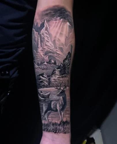 Tatuaj realist cu peisaj montan și cerb pe antebraț