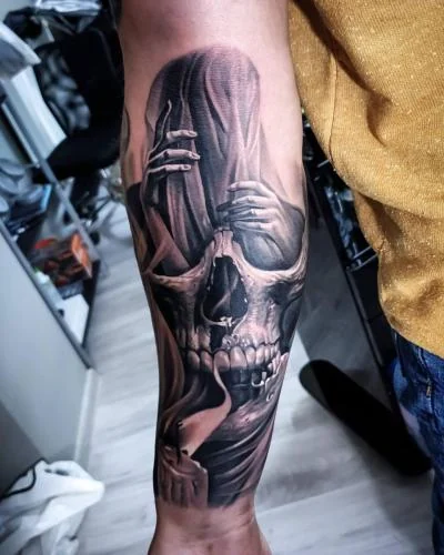 Tatuaj realist cu craniu și mâini pe antebraț