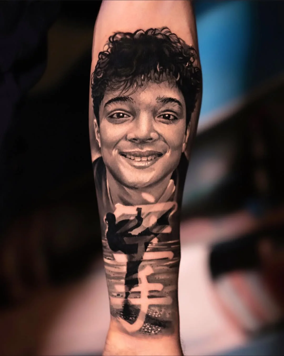 Tatuaj realist cu portret de băiat zâmbitor și siluetă pe antebraț
