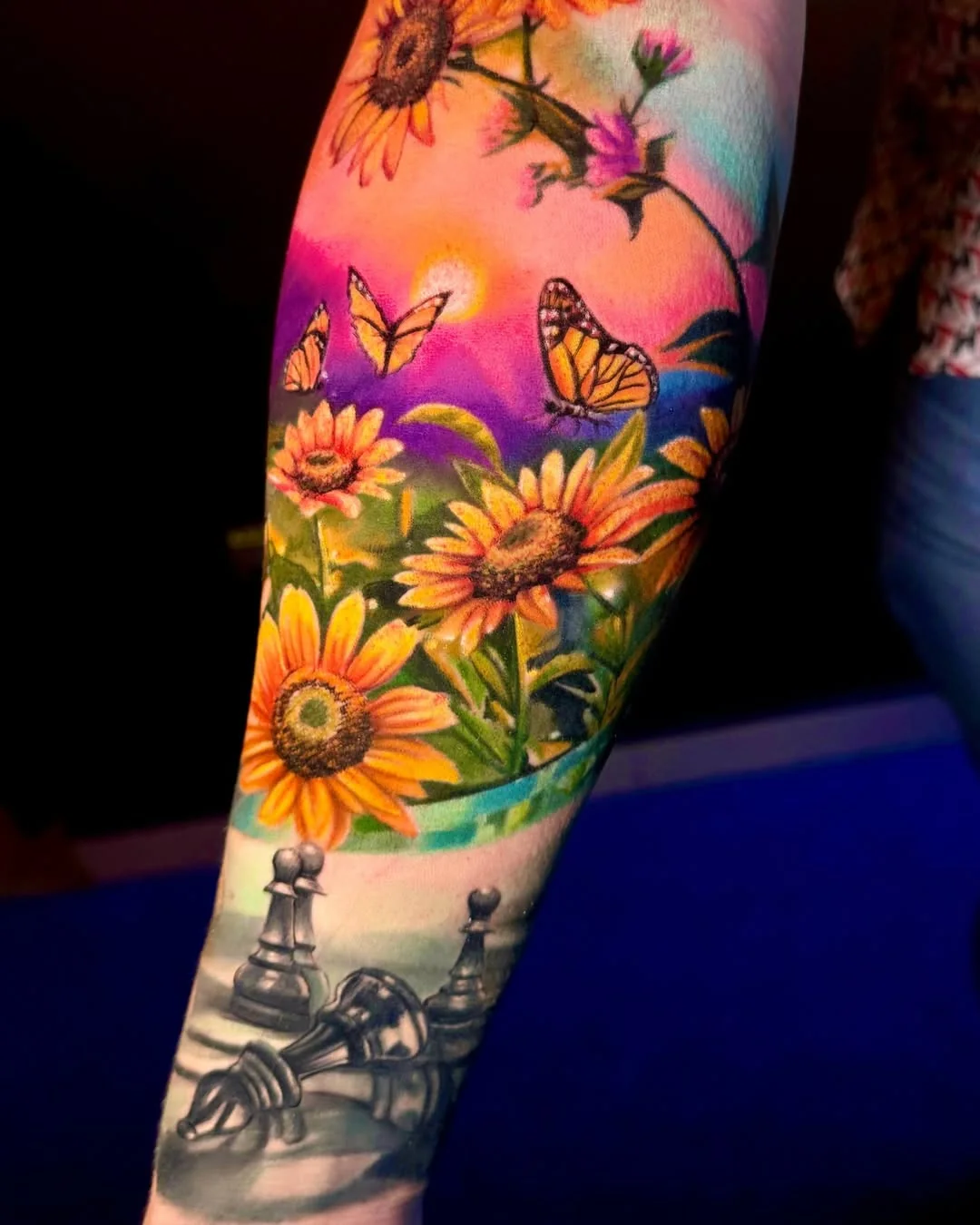 Tatuaj color cu floarea-soarelui, fluturi și piese de șah pe antebraț